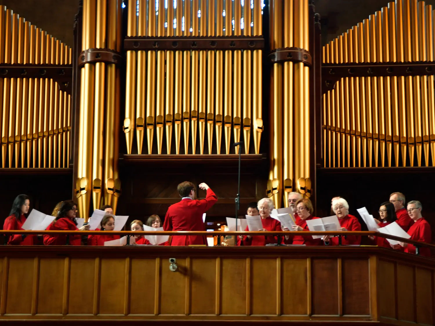 The choir in red robes singing before the gilded organ pipes in the west gallery