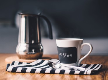 A stovetop coffee pot and a mug labelled 'coffee' on a striped cloth