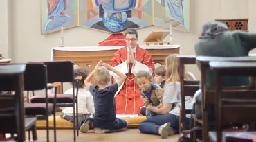 A priest in red vestments blesses children gathered around the altar