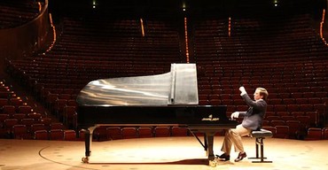 A pianist playing a grand piano alone on a concert hall stage