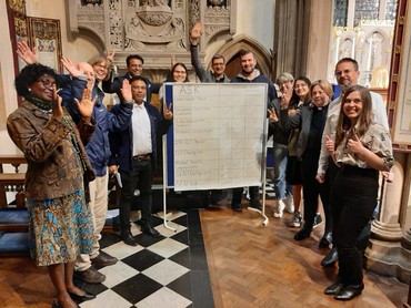 Parishioners and fellow Citizens UK members celebrate together in church beside a flipchart of commitments