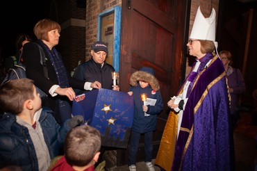 A bishop in purple vestments greets children holding lit candles outdoors at night