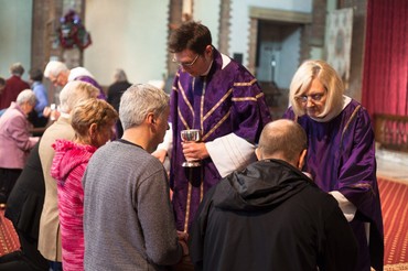 A priest in purple vestments gives communion to kneeling worshippers at the altar rail