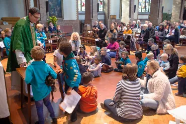 A priest in a green chasuble leads children gathered around the altar