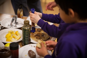 A child adding a topping to pancakes at a shared breakfast table