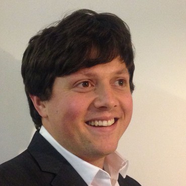 Daniel Mackintosh smiling, in a dark suit and pale shirt