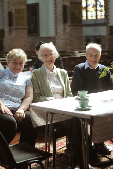 Three people chatting over tea at a table in the church