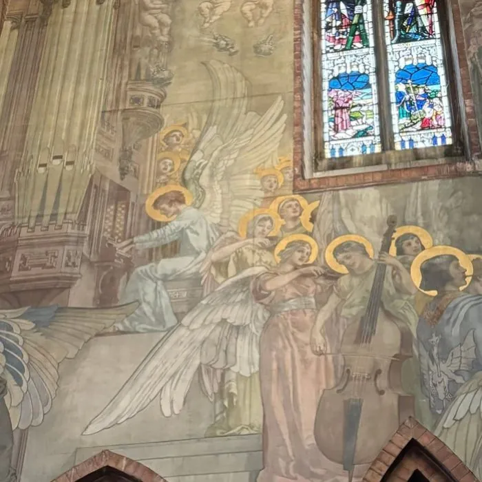 A mural of angel musicians beside a stained glass window inside the church