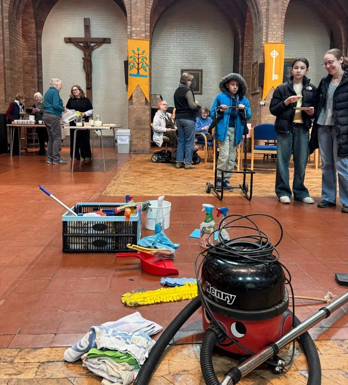 Volunteers and children clean the church floor with mops, buckets and a vacuum cleaner