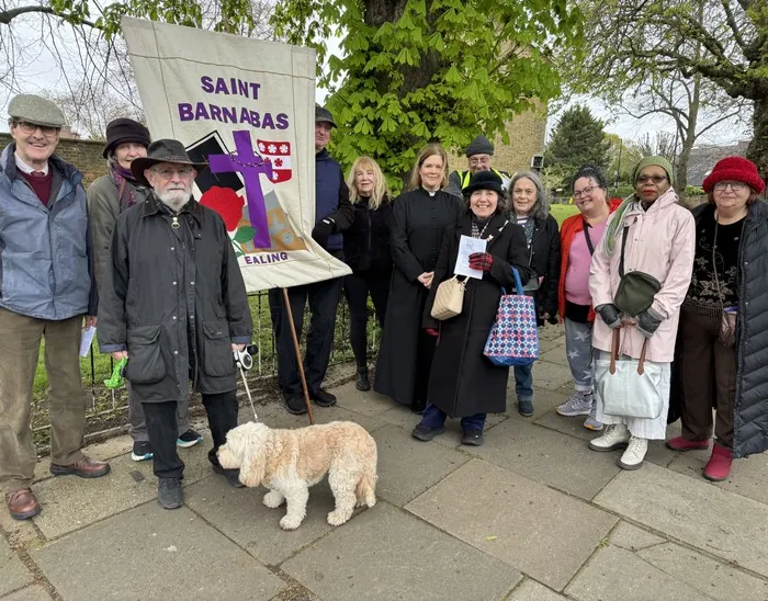 A group holding a St Barnabas parish banner gather outdoors with a dog