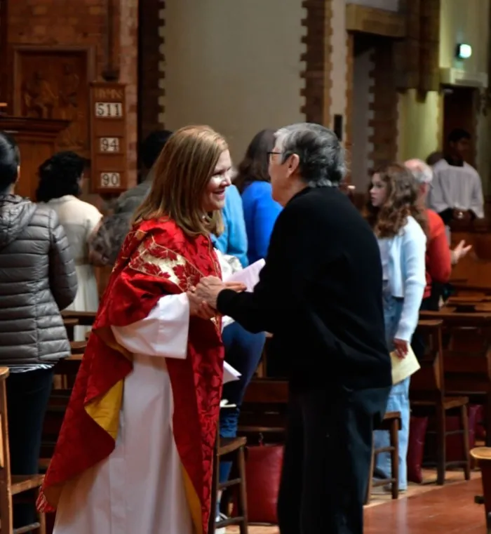 A priest in red and gold vestments greets a parishioner in the church