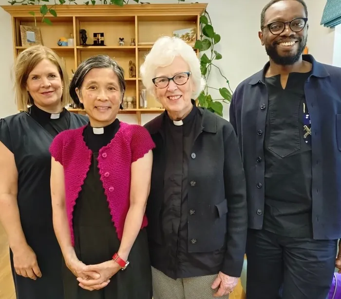 Three women in clerical collars and a man smiling together indoors