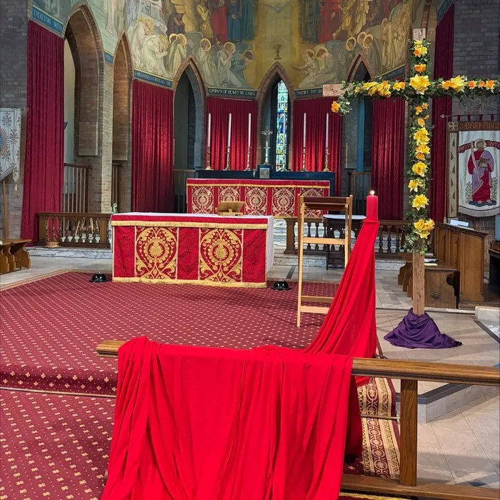 The sanctuary dressed in red for Pentecost, with a flower-covered cross beside the altar