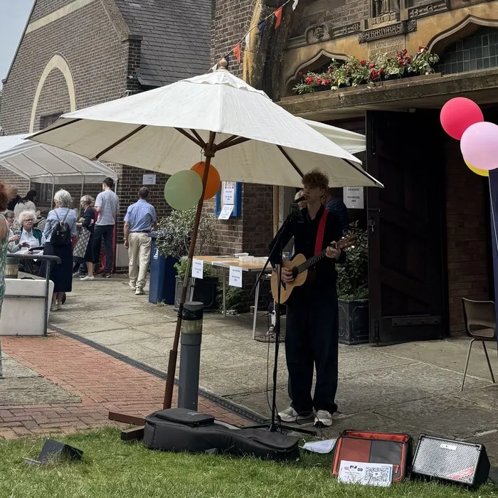 A musician playing guitar under a parasol at the Summer Fayre