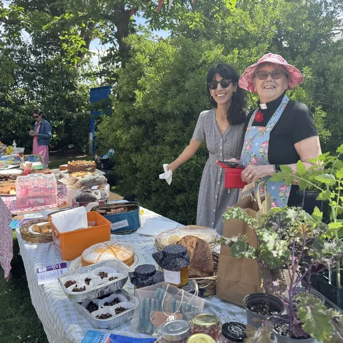 Two women smiling behind a stall of cakes and preserves at the Fayre