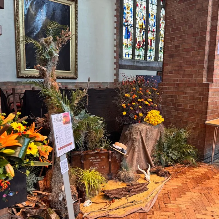 A film-themed flower display with palm fronds, a travel trunk and an animal skull evoking a desert scene