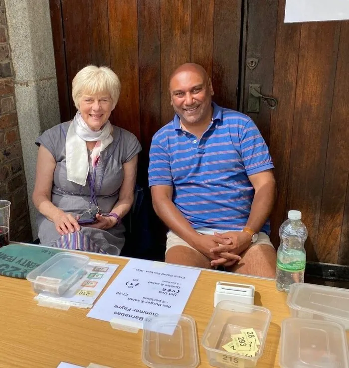 Sanjit sitting at a stall table during the Summer Fayre, smiling with a colleague