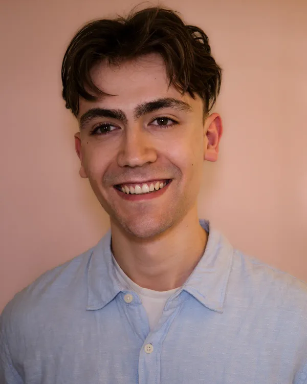 Luca smiling in an open-collared pale blue shirt