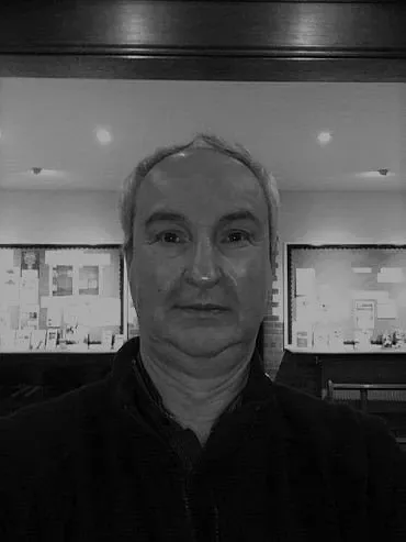 Nick in the church foyer with the parish noticeboards behind him, in a black-and-white photograph